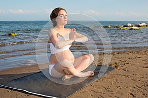 Pregnant woman doing exercise on yoga pose on ocea