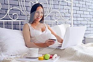 Pregnant woman doing online shopping in the bedroom