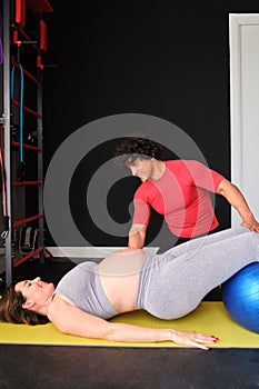 Pregnant woman doing Pilates exercise with a fitball with personal trainer.