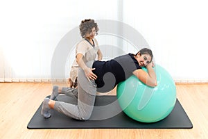 A pregnant woman doing pilates exercises with a ball with the help of her physiotherapist