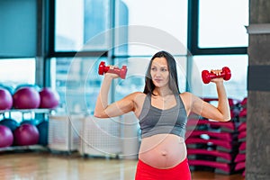 pregnant woman doing sport exercises in gym with red dumbbells
