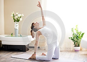 Pregnant woman doing ustrasana yoga pose at home