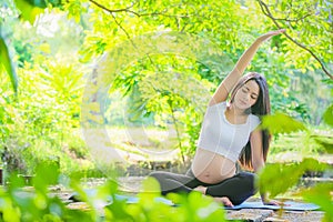 Pregnant woman doing yoga exercise in nature on summer