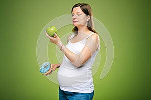 Pregnant woman with donut and green apple, advice which products you should eat. Healthy lifestyle on perinatal time.