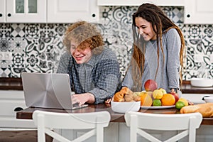 Pregnant woman with dreadlocks and her curly husband in modern kitchen cooking behind. Fresh and healthy food concept.