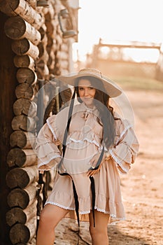 a pregnant woman in a dress and hat in the countryside holds a horse bridle in her hand