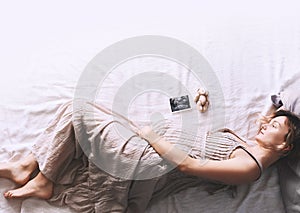 Pregnant woman in dress holding hands on belly lying on side in profile in bed.  Expectant mother waiting for baby birth during