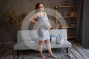 Pregnant woman in a dress holding her hands on stomach in the living room interior. Pregnancy, motherhood, preparation