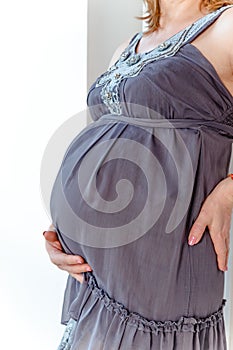 Pregnant woman in dress holds hands on belly on a white background. Pregnancy, maternity, preparation and expectation