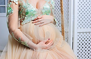 Pregnant woman in dress holds hands on belly on a white background. Pregnancy, maternity, preparation and expectation concept. Clo