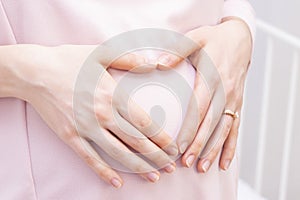 Pregnant woman in a dress holds her hands on her stomach in the shape of a heart. The concept of pregnancy, motherhood,