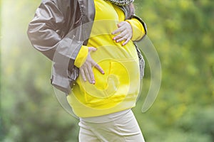 Pregnant woman dressed a hoodie and jacket holds hands on belly on a green background. Pregnancy, maternity