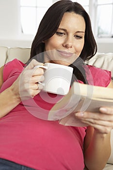 Pregnant Woman Drinking Hot Drink And Reading Book At Home