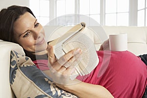 Pregnant Woman Drinking Hot Drink And Reading Book At Home