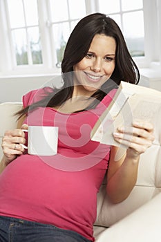 Pregnant Woman Drinking Hot Drink And Reading Book At Home