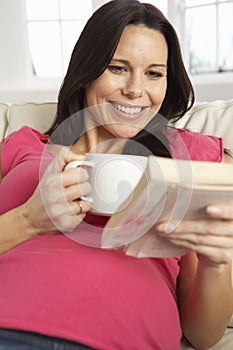 Pregnant Woman Drinking Hot Drink And Reading Book At Home