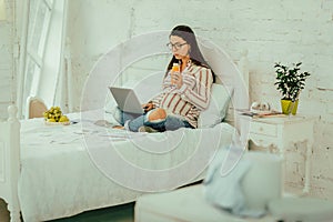 Pregnant woman drinking a juice and working remotely