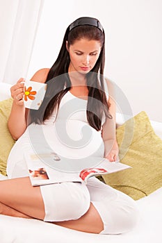 Pregnant woman drinking tea and reading magazine