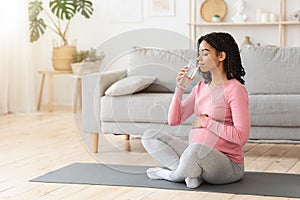 Pregnant woman drinking water during exercising at home