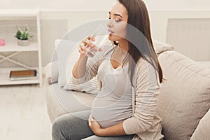 Pregnant woman drinking water sitting on sofa