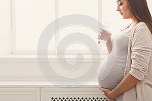 Pregnant woman drinking water at window