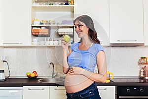 Pregnant woman eating an apple at home in the kitchen