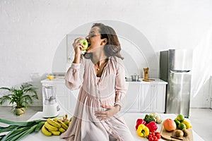 Pregnant woman eating apple near food on table