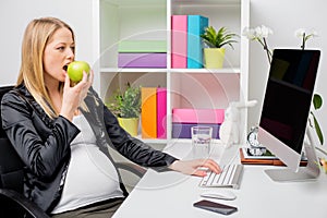 Pregnant woman eating apple at the office