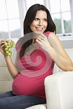 Pregnant Woman Eating Grapes Sitting On Sofa At Home