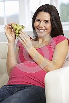 Pregnant Woman Eating Grapes Sitting On Sofa At Home