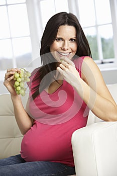 Pregnant Woman Eating Grapes Sitting On Sofa At Home