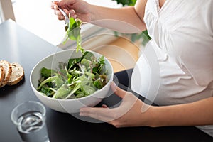 Pregnant woman eating a green salad at home