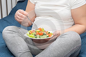 A pregnant woman is eating a healthy homemade organic fruit salad while sitting on her bed.