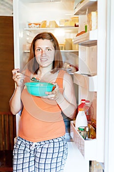 Pregnant woman eating near refrigerator at