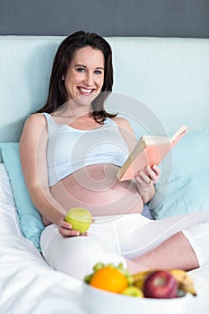 Pregnant woman eating and reading book