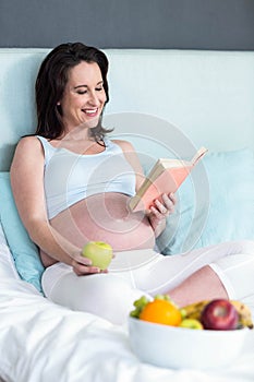 Pregnant woman eating and reading book