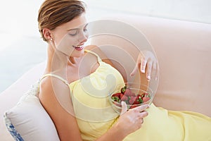Pregnant woman, eating strawberries and happy in home, alone and enjoying delicious pregnancy craving. Good mood, fruit