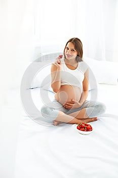 Pregnant Woman Eating Strawberry at home. Healthy Food Concept.