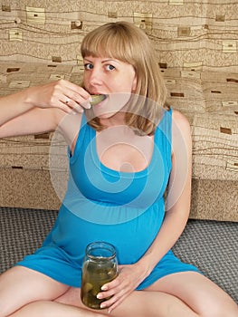 The pregnant woman eats pickle, sitting on a floor. Toxicosis photo