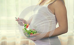 A pregnant woman eats a salad with vegetables. Selective focus