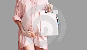 Pregnant woman with empty white paper as medical card, agreement blank. Template for text