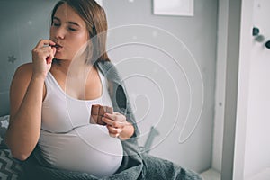 Pregnant woman enjoying of eating chocolate at home.