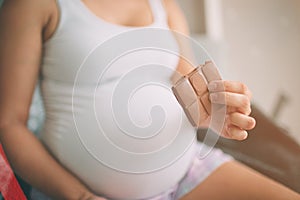 Pregnant woman enjoying of eating chocolate at home.