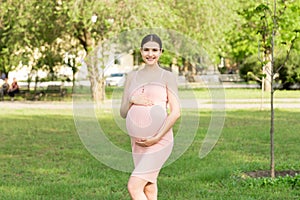 Pregnant woman enjoying and relaxing outside in the park. Pregnancy, maternity and happiness