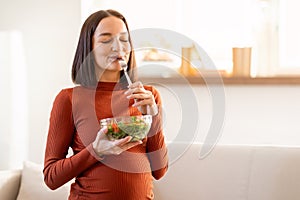 Pregnant woman enjoying vegetable salad meal posing with bowl indoor