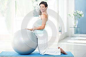 Pregnant woman with exercise ball kneeing on mat photo