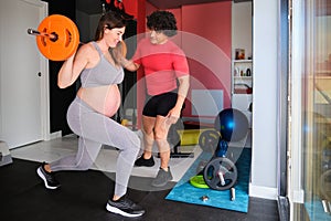 Pregnant woman exercising with a barbell with personal trainer's help.