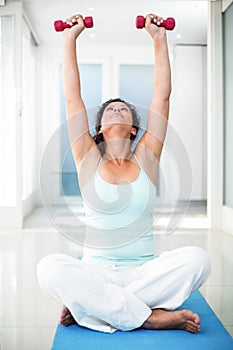 Pregnant woman exercising with dumbbells while sitting on exercise mat