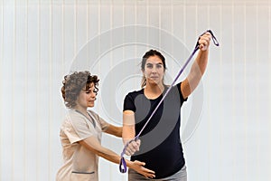 A pregnant woman exercising with an elastic band with help of physiotherapist