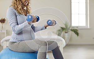 Pregnant woman exercising with fit ball and dumbbells during pregnancy workout at home